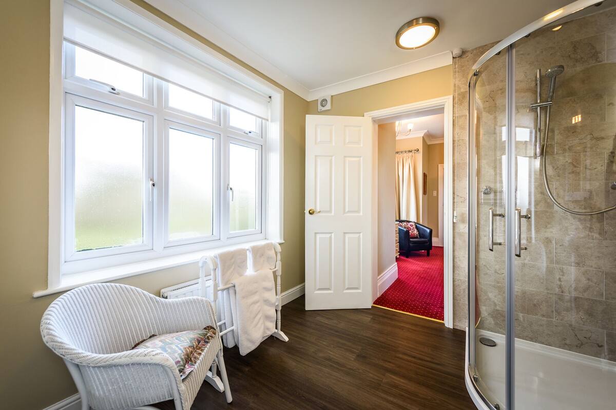 A bathroom with a glass shower, a white door, and a wicker chair.