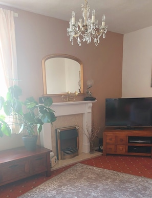 A living room with a fireplace, a television, a chandelier, and a mirror. - Two Beaches (Paignton)