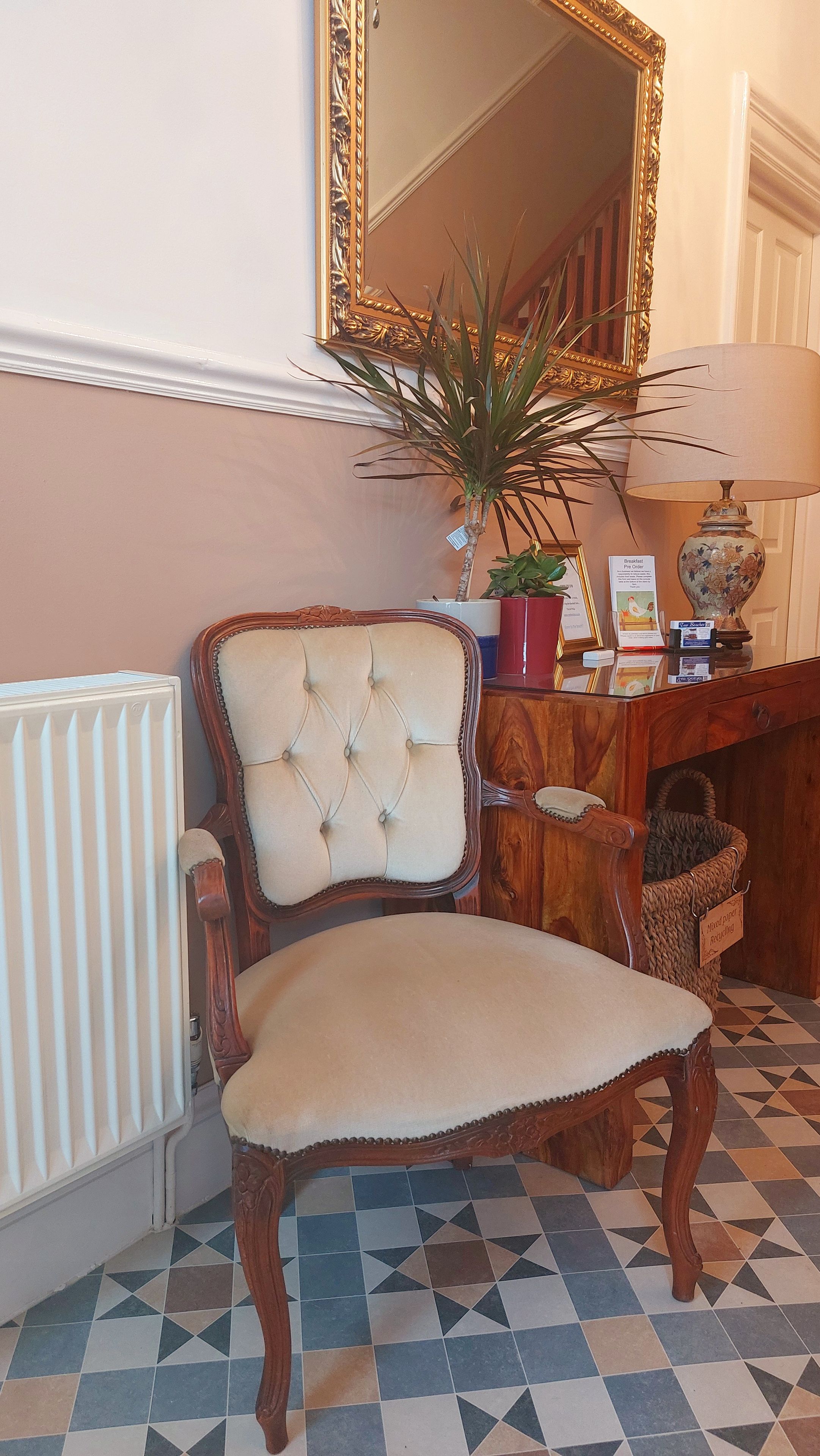 A room with a tufted armchair, a radiator, a potted plant, a fireplace, and a tiled floor.