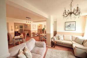 A spacious living area with a sofa, a dining table, and a chandelier. - Two Beaches (Paignton)