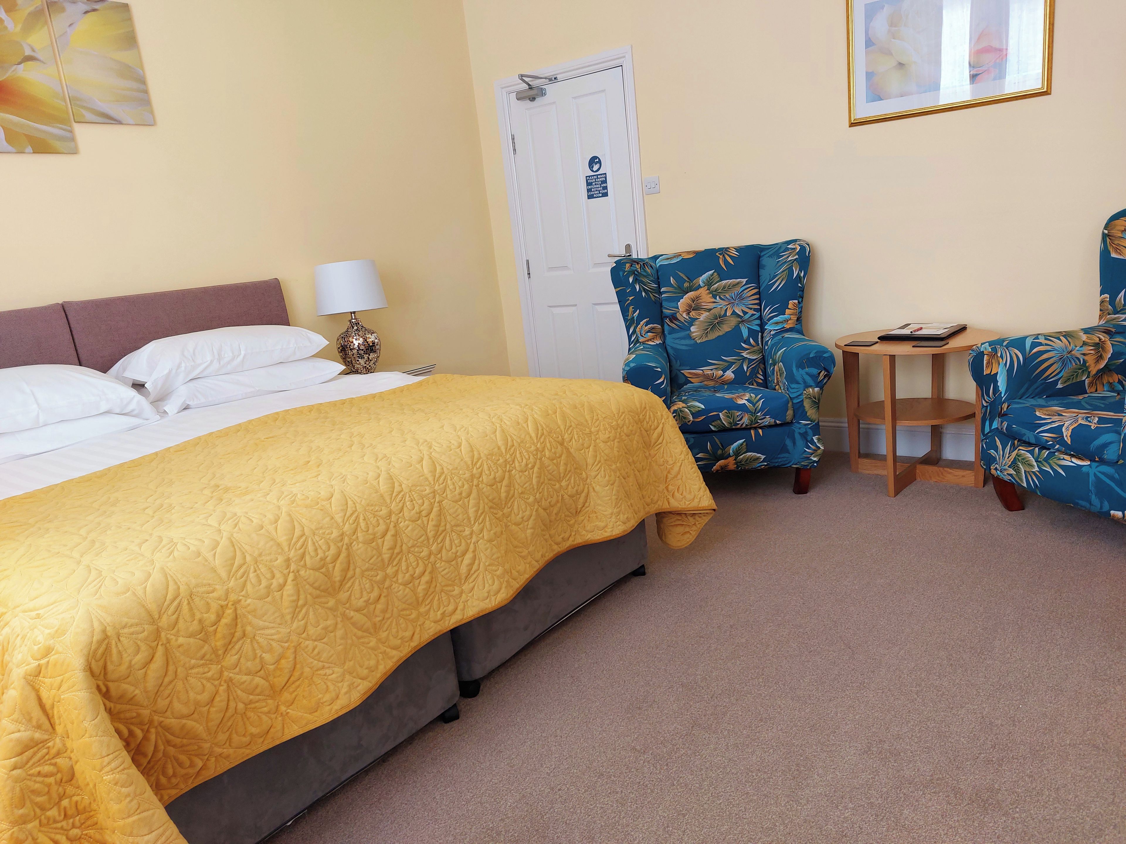 A hotel room with a bed, a chair, a small table, and a door.