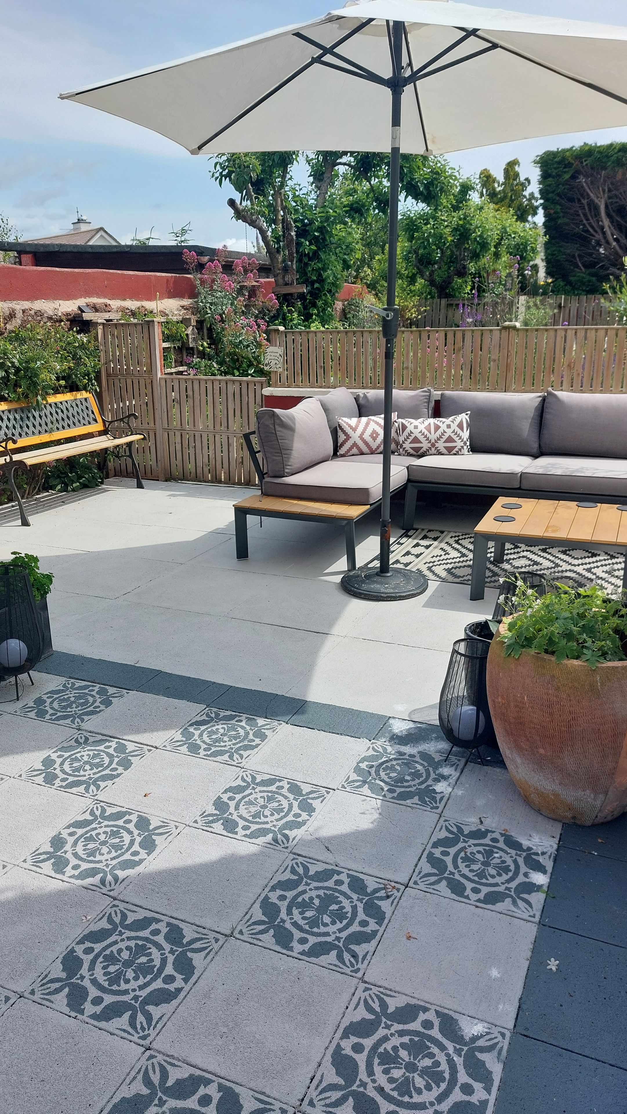 An outdoor patio with a sofa, a wooden table, a bench, and a large umbrella.