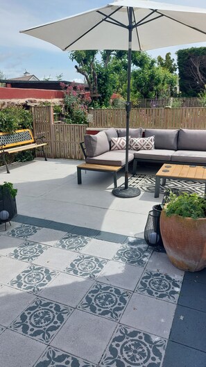 An outdoor patio with a sofa, a wooden table, a bench, and a large umbrella. - Two Beaches (Paignton)