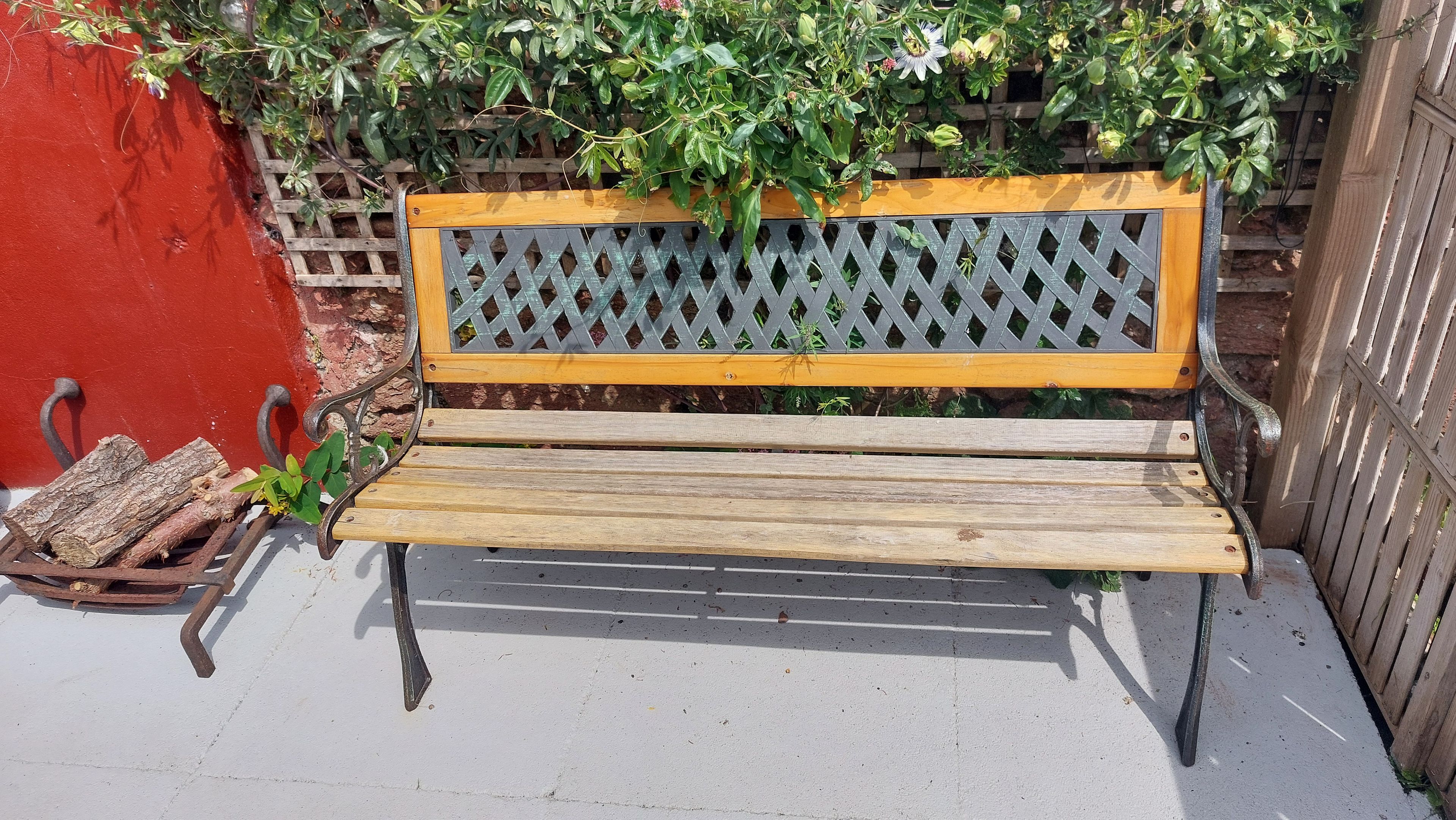 A wooden bench with metal armrests and a lattice backrest, placed on a concrete surface.