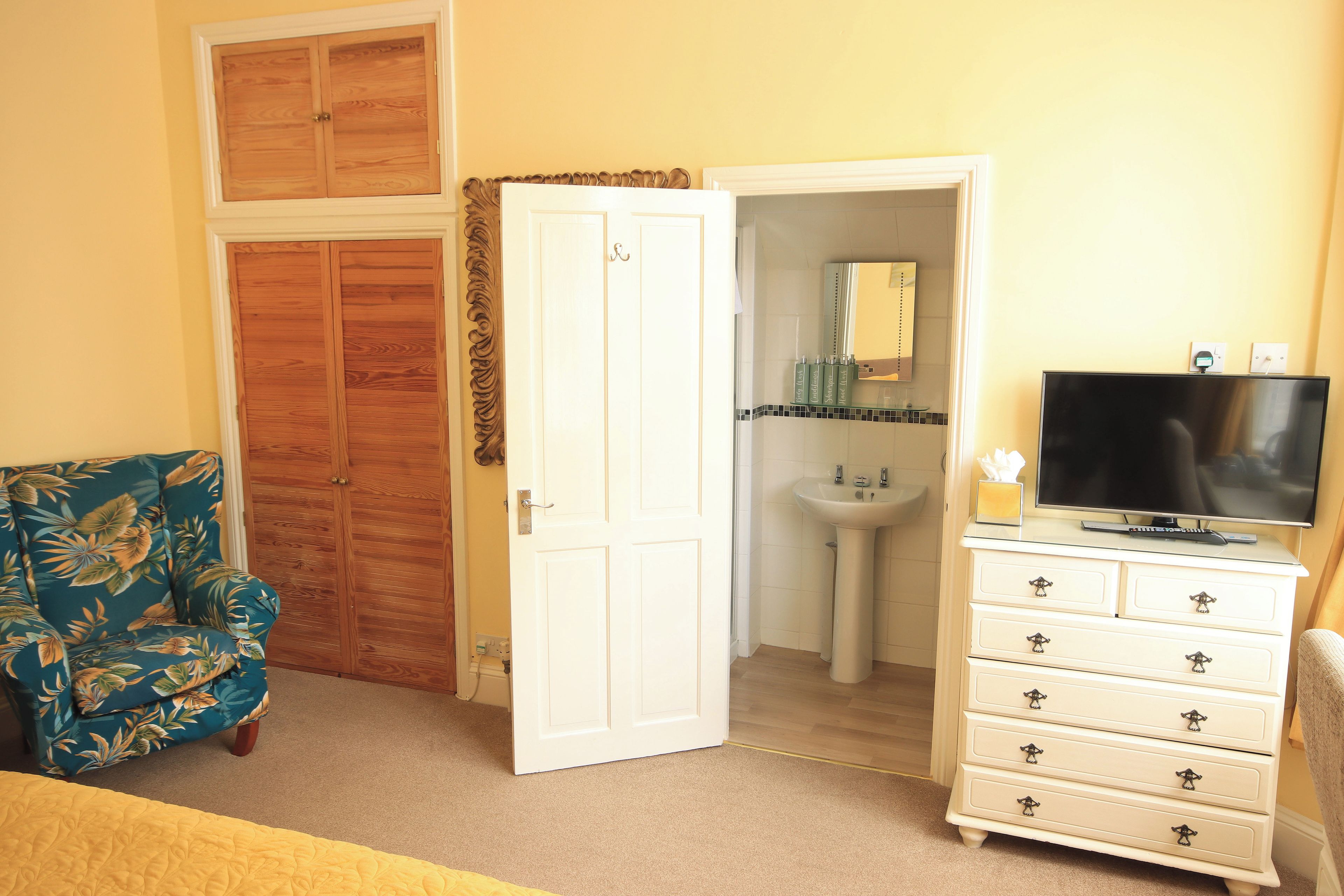 A room with a bed, a chair, a dresser, a television, and a bathroom visible through an open door.