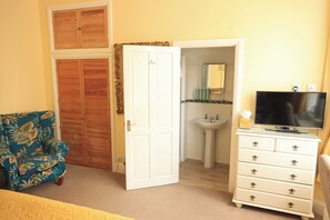 A room with a bed, a chair, a dresser, a television, and a bathroom visible through an open door. - Two Beaches (Paignton)