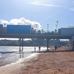 Une plage avec une jetée, des gens qui se promènent et un panneau indiquant « Glace pilée très froide ».