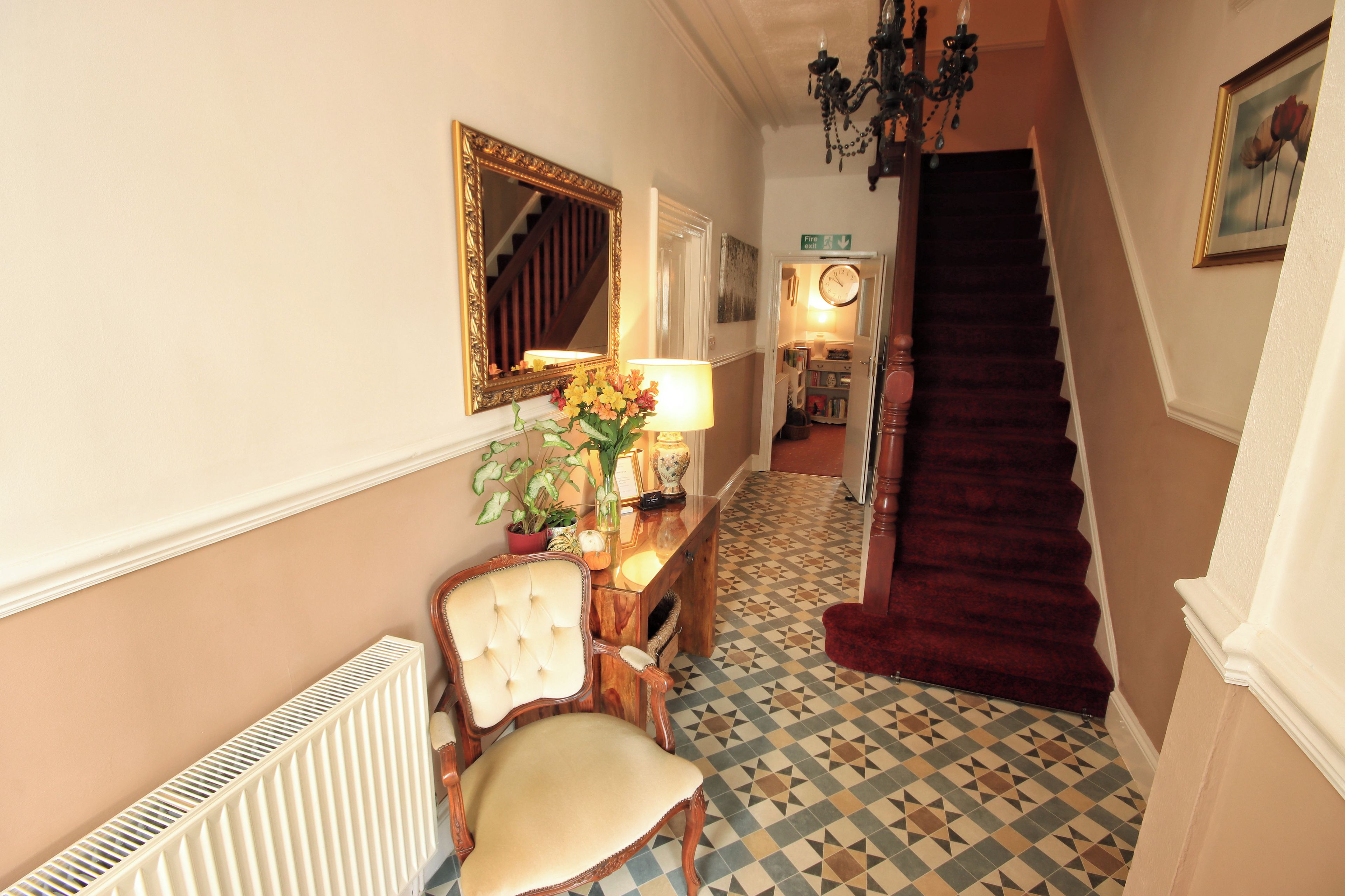 A hallway with a chair, a mirror, a lamp, and a staircase.