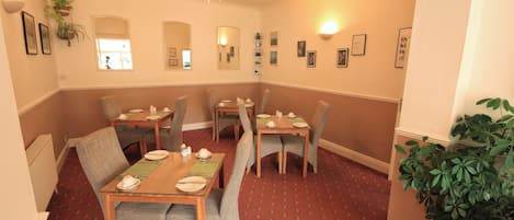 A dining area with multiple tables and chairs, a ceiling light, and framed pictures on the walls.