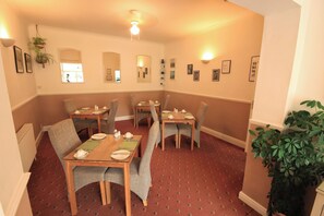 A dining area with multiple tables and chairs, a ceiling light, and framed pictures on the walls. - Two Beaches (Paignton)