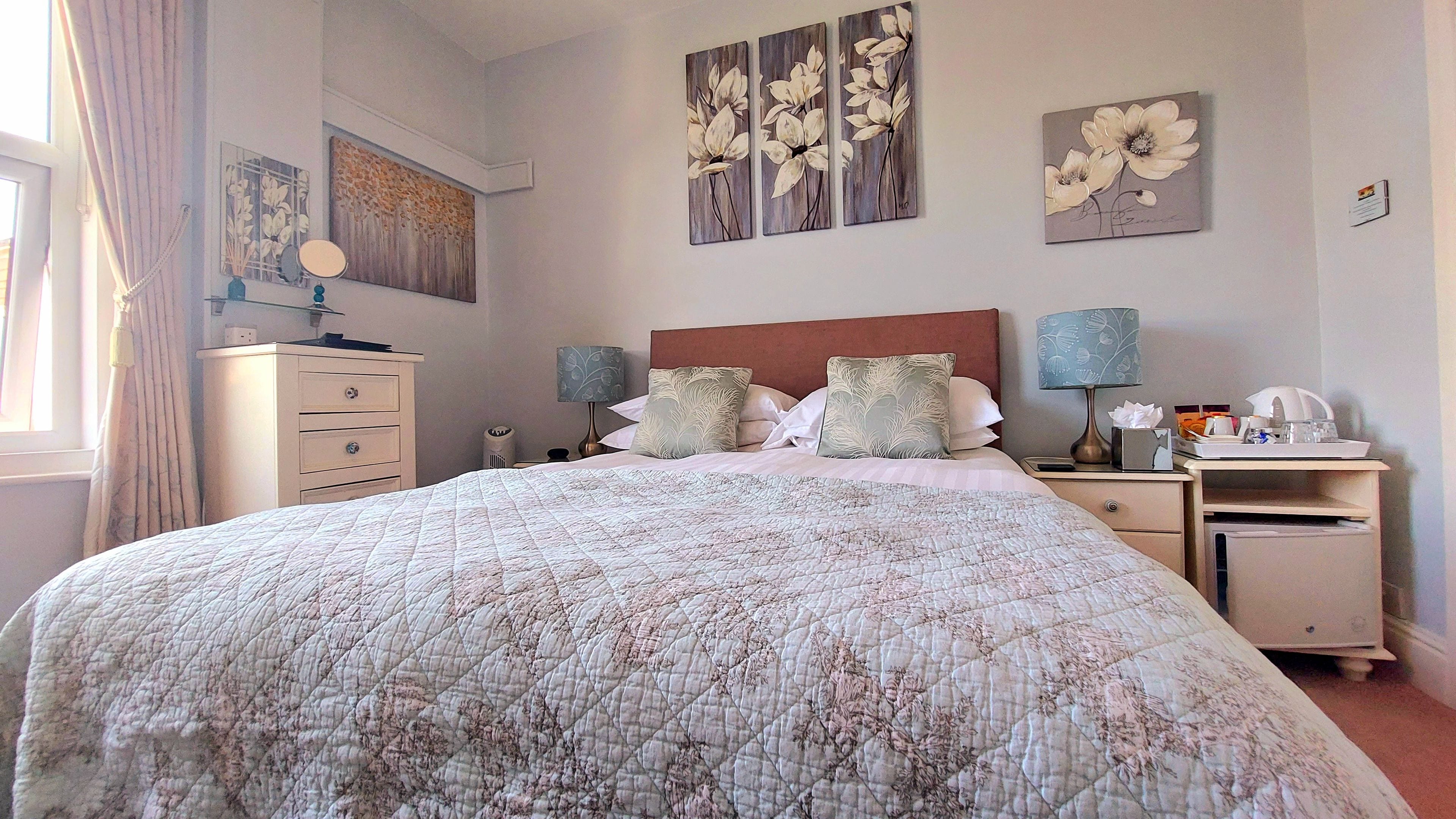 A neatly arranged bedroom with a large bed, bedside tables, a dresser, and artwork on the walls.
