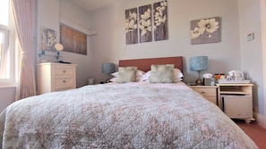 Ein ordentlich eingerichtetes Schlafzimmer mit einem großen Bett, Nachttischen, einer Kommode und Kunstwerken an den Wänden.