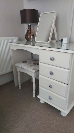 A white desk with a lamp, a mirror, and a chair with floral upholstery.