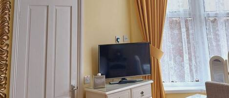 Una habitación con ventilador de techo, televisor sobre una cómoda, una puerta y una ventana con cortinas.