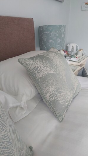 Un letto rifatto con un cuscino a fiori grigio, un cuscino bianco e una testiera marrone.