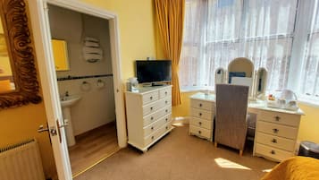 A hotel room with a bathroom, a television, a vanity with a mirror, and a window with curtains.