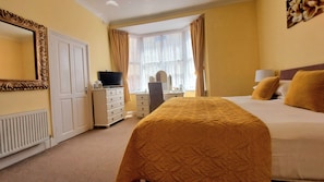 A hotel room with a bed, a dresser, a television, and a window with curtains.