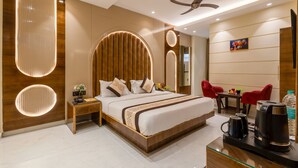 Una habitación de hotel moderna con una cama grande, un escritorio con cafetera y una zona de estar con sillas rojas.