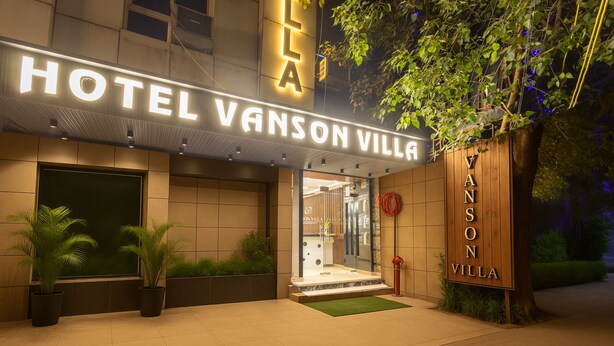 Exterior del Hotel Vanson Villa con una entrada bien iluminada, plantas en macetas y un letrero de madera.