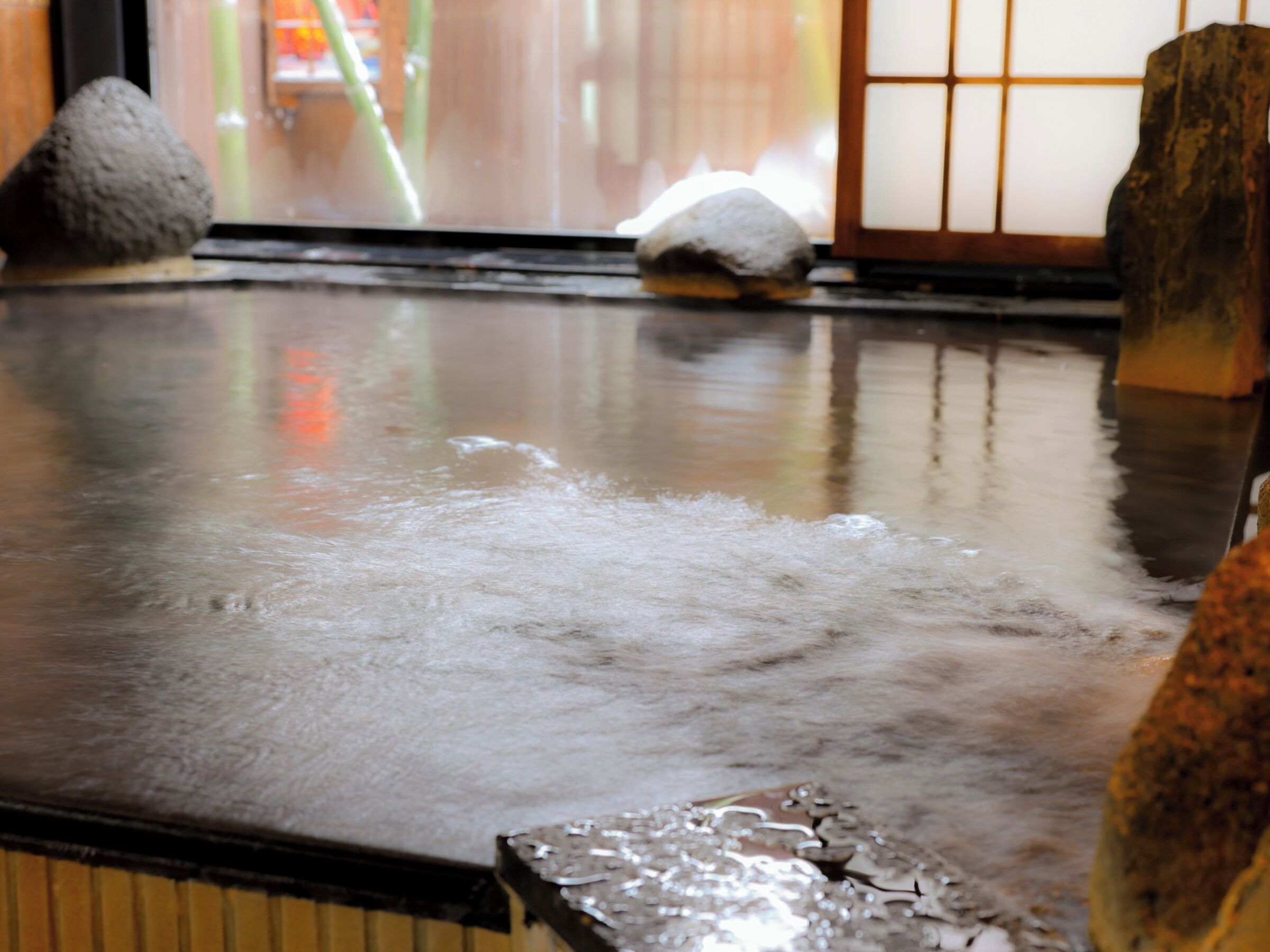 Un onsen japonés tradicional con suelo de madera, asientos de piedra y vistas a una estructura de bambú.