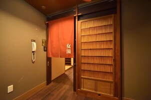 Un pasillo con una puerta de madera, un teléfono y un estandarte rojo con caracteres japoneses.