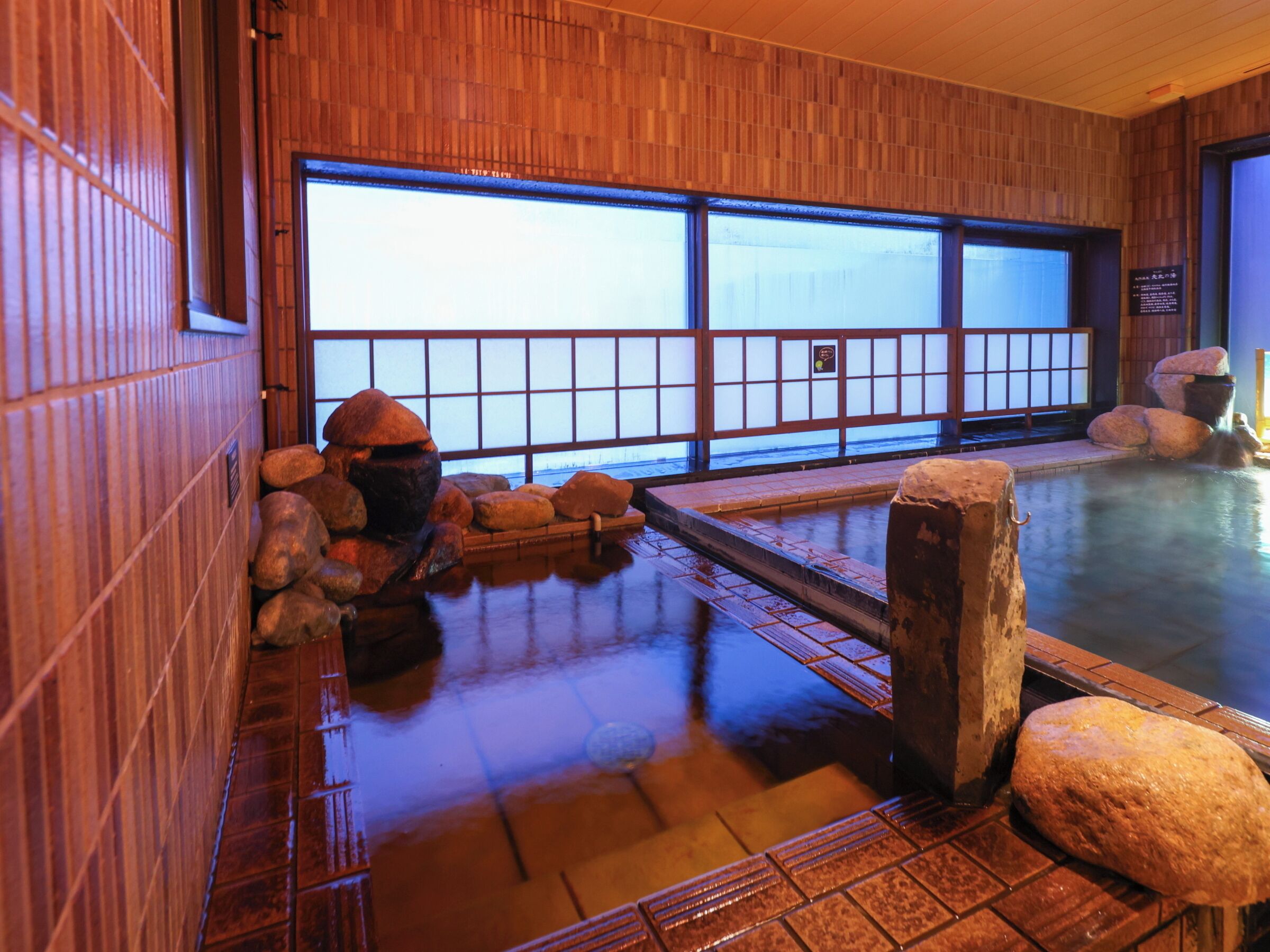 A traditional Japanese onsen with wooden walls, a stone bath, and a view through shoji screens.