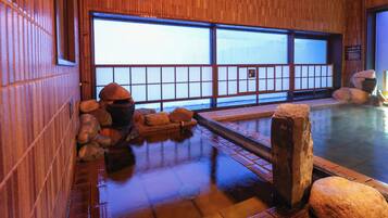 A traditional Japanese onsen with wooden walls, a stone bath, and a view through shoji screens.