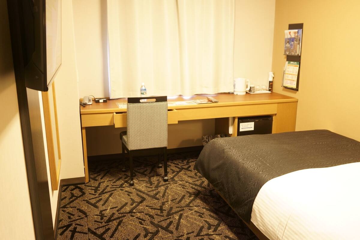 A hotel room with a bed, a desk, a chair, a television, and a window with curtains.
