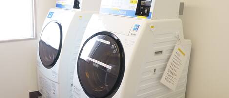 A row of front-loading washing machines in a laundry room with a window and wooden flooring.