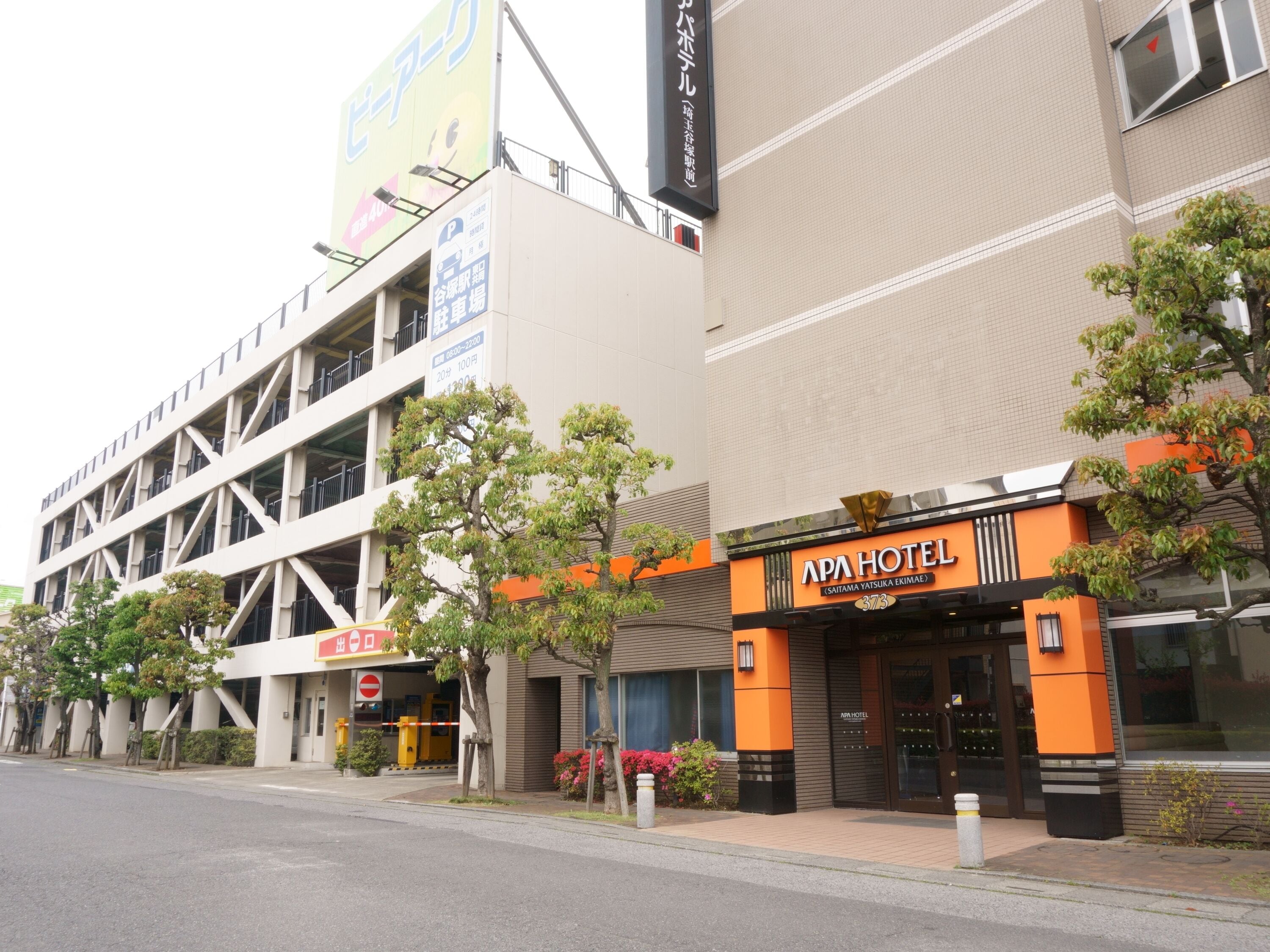 Un bâtiment moderne avec une enseigne indiquant « APA HOTEL (SAITAMA YATSUKA EKIMAE) » et un parking.