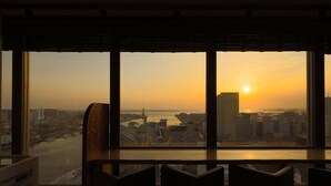 A room with a large window overlooking a cityscape at sunset, featuring modern chairs and a wooden desk. - Natural Hot Spring Dormy Inn Premium Kushiro (Kushiro)
