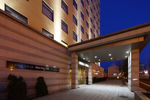 Entrada de un hotel con un letrero que dice "dormy inn Premium" y un corredor cubierto que lleva a la entrada.