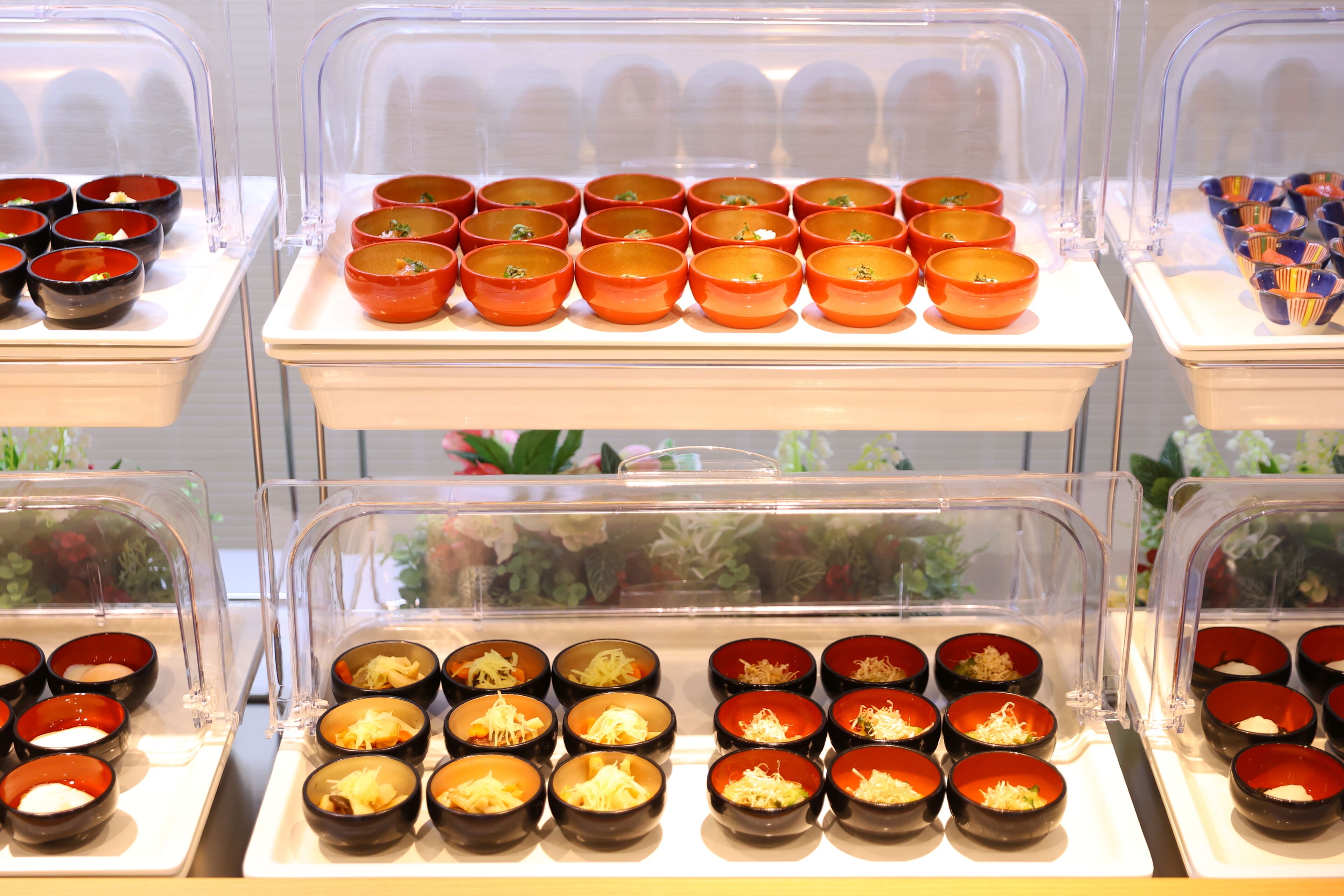 A buffet with multiple bowls of food, each with a clear plastic cover.