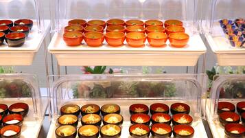 A buffet with multiple bowls of food, each with a clear plastic cover.