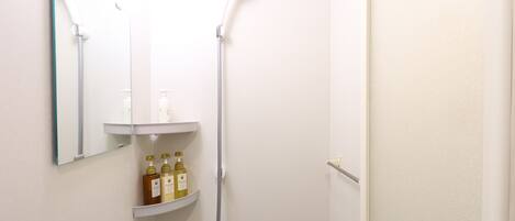 A small, white bathroom with a shower, a mirror, and a shelf with toiletries.