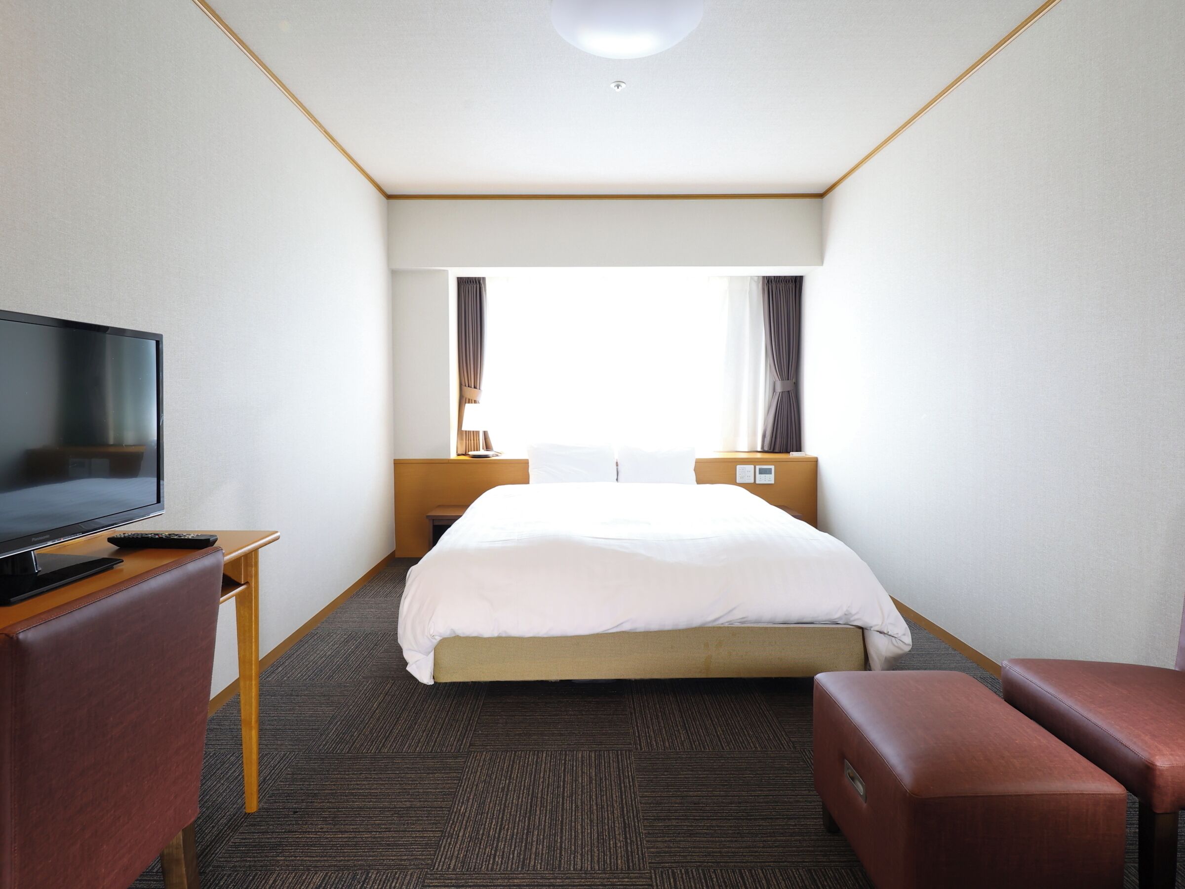 Habitación de hotel con cama, televisión, escritorio y ventana con cortinas.