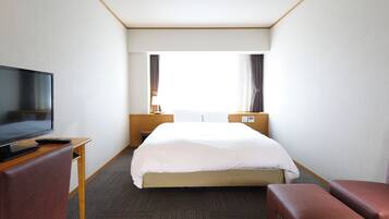 Habitación de hotel con cama, televisión, escritorio y ventana con cortinas.