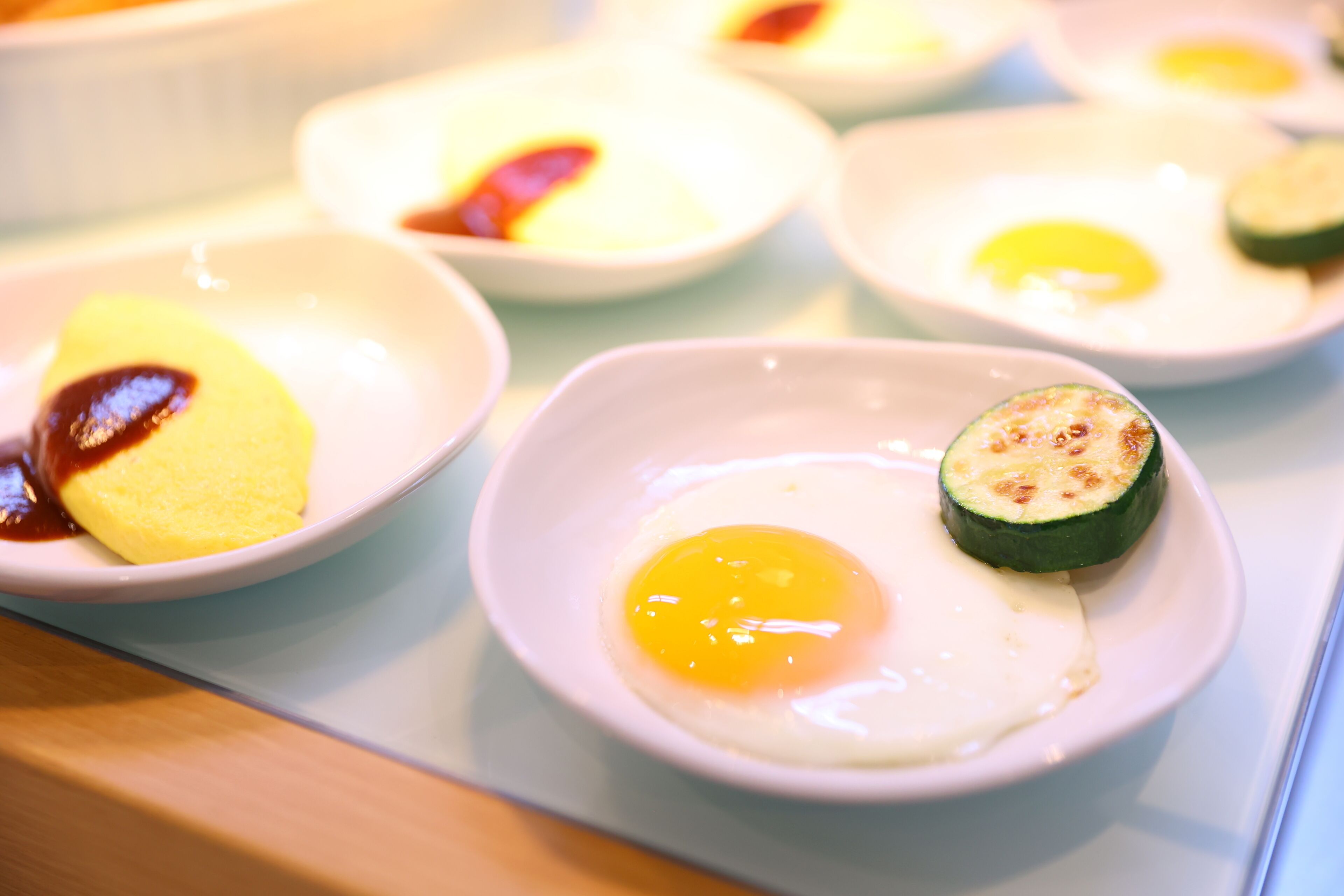 A table with several small white dishes containing eggs and slices of zucchini.