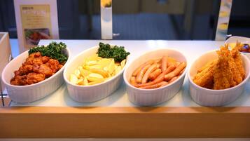 A food display with four dishes: fried chicken, potatoes, sausages, and fried fish.