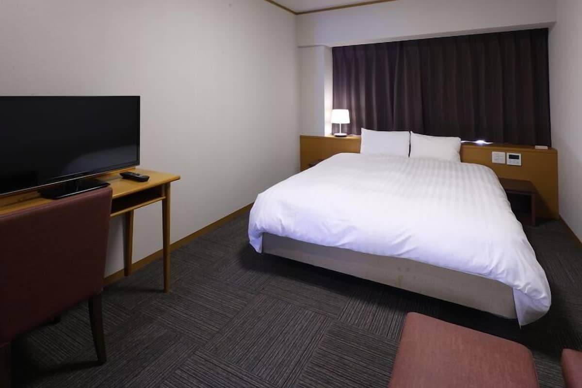 Ett hotellrum med en säng, en TV, ett skrivbord och en stol.
