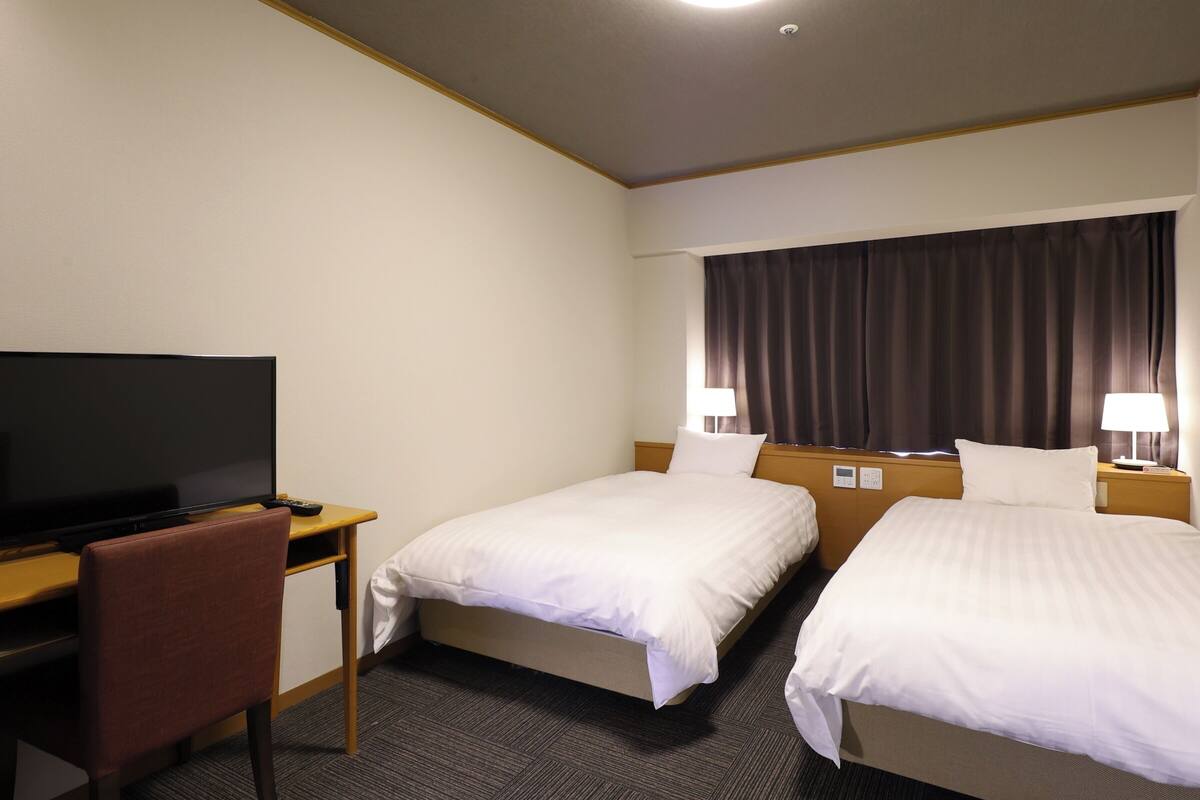 A hotel room with two single beds, a desk with a television, and a chair.