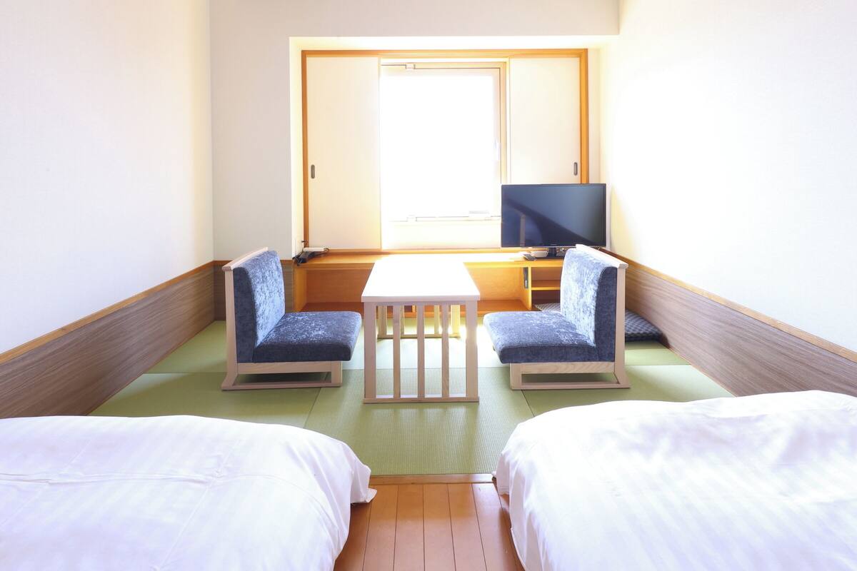 A hotel room with two beds, a small table, two chairs, a television, and a sliding door.