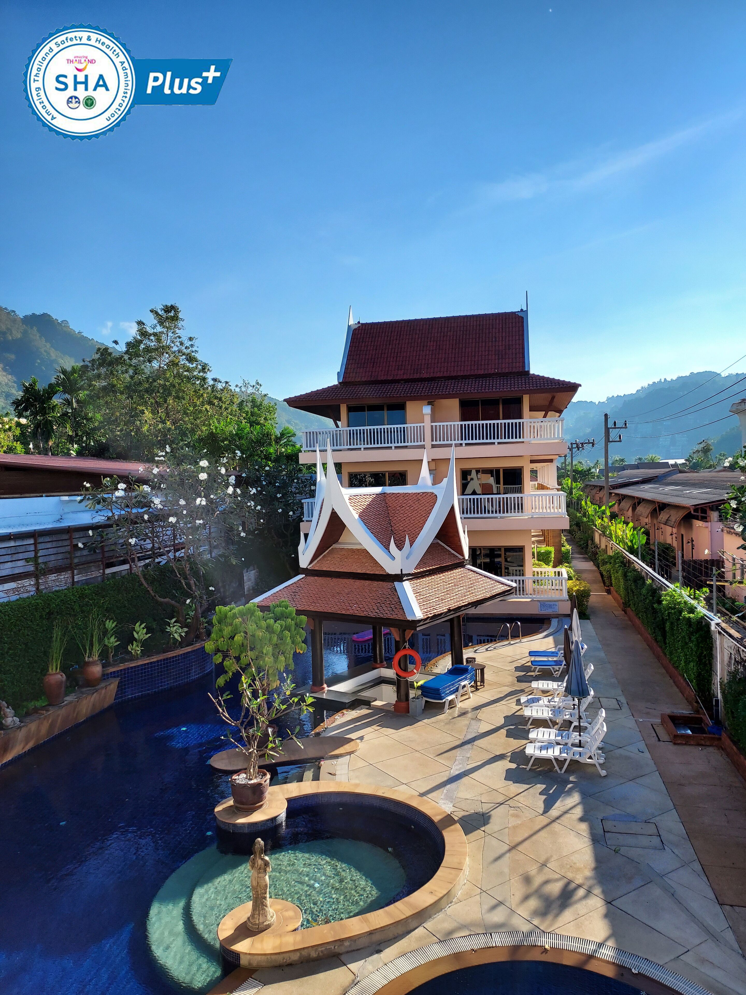 A hotel with a traditional architectural style, featuring a large building with multiple balconies and a swimming pool area with lounge chairs and a statue.