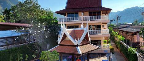 A hotel with a traditional architectural style, featuring a large building with multiple balconies and a swimming pool area with lounge chairs and a statue.