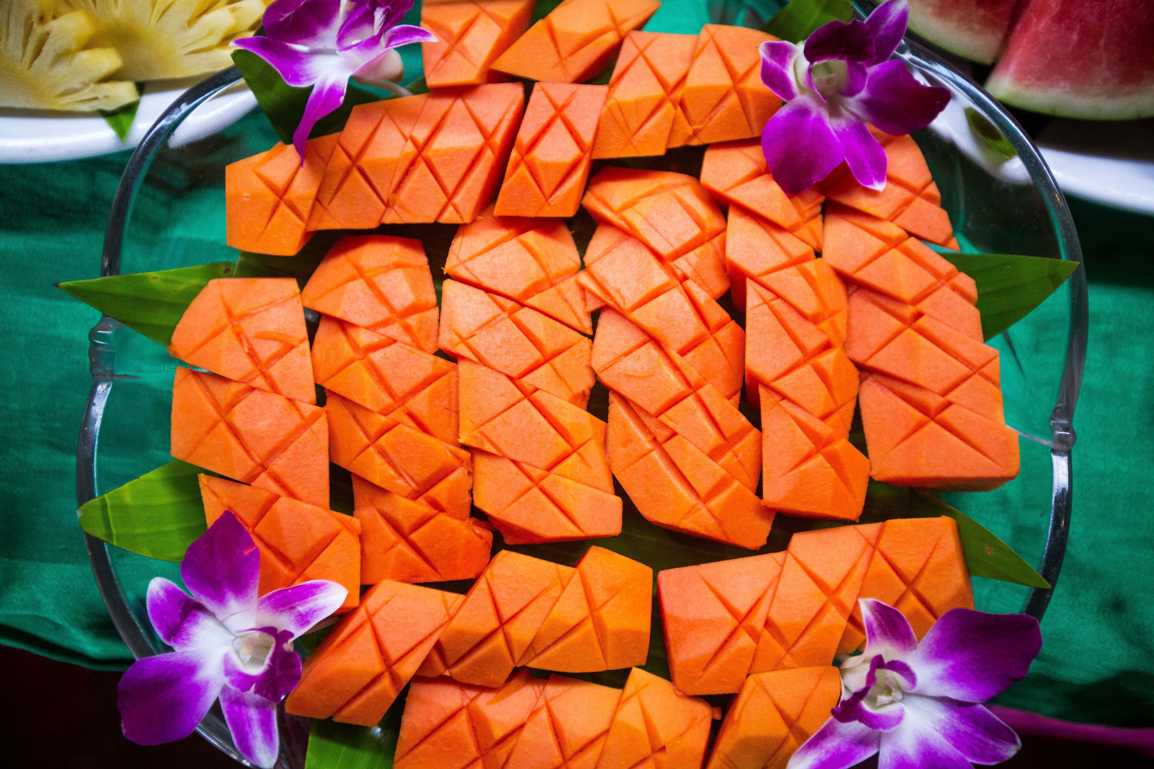 A glass bowl filled with cubed mangoes, surrounded by purple orchids.