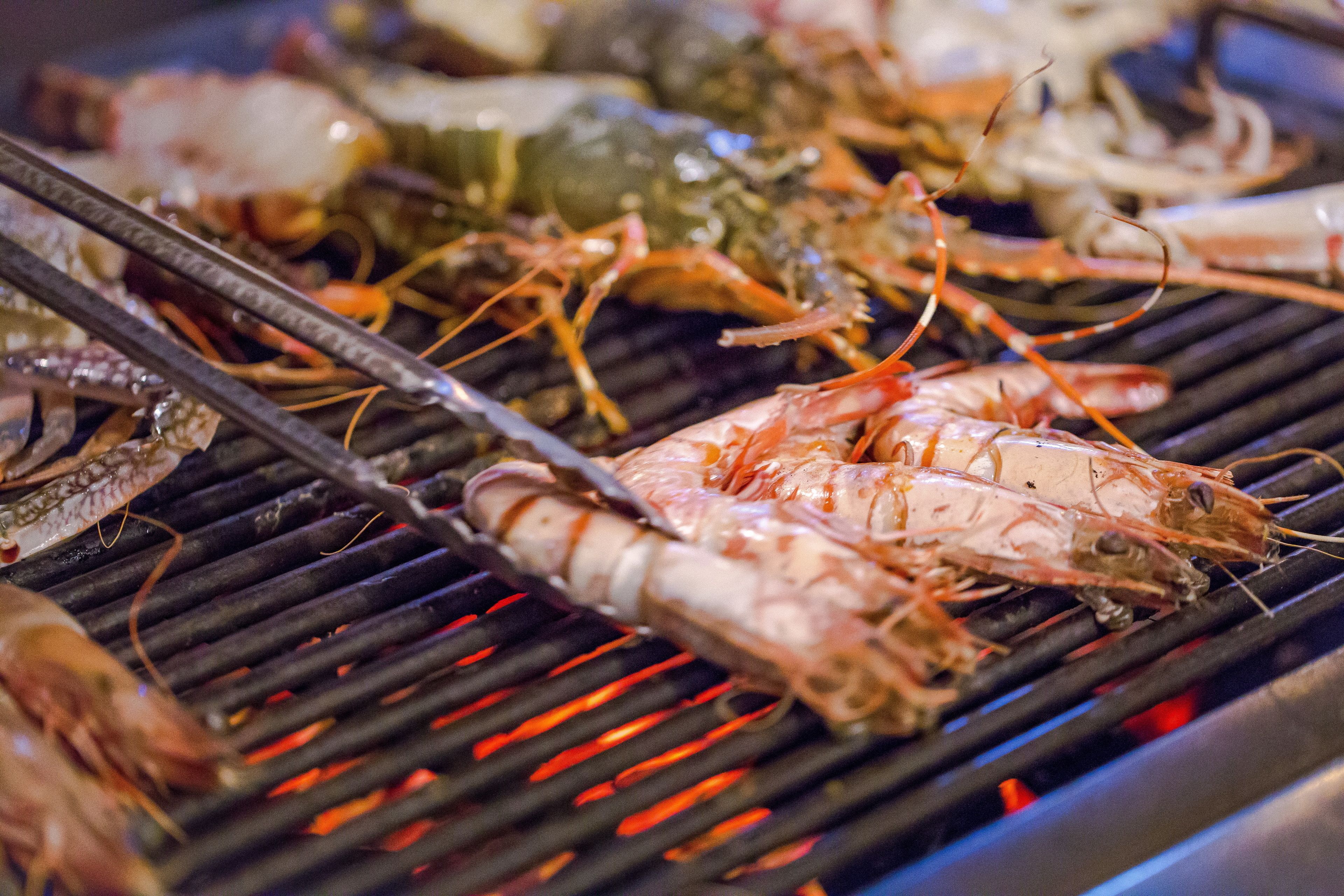 A grill with various seafood, including shrimp and lobster, being cooked.