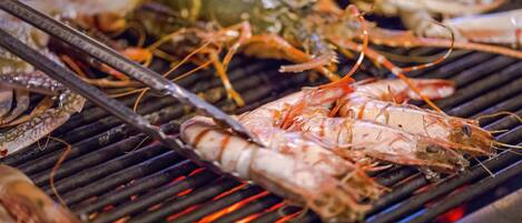 A grill with various seafood, including shrimp and lobster, being cooked.