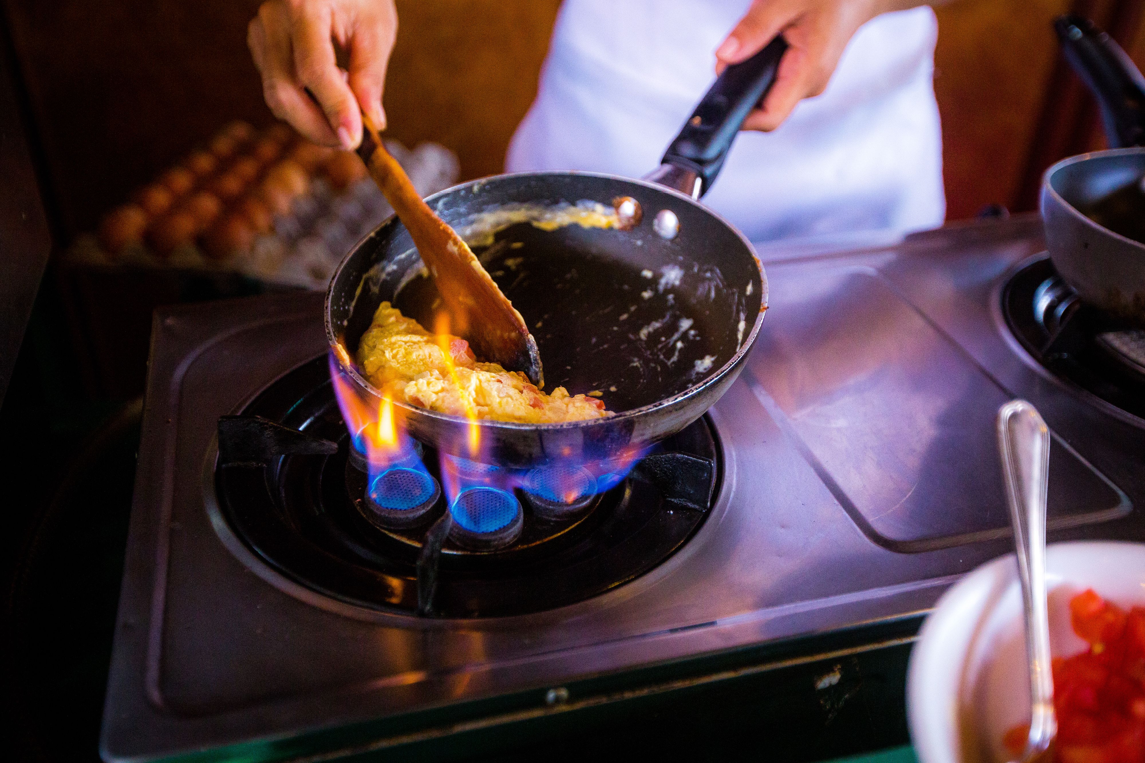 A person cooking on a stove with a frying pan.