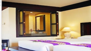 A hotel room with two beds, a large mirror, a bedside table with a lamp, and a small table with a vase of flowers. - Kata Poolside Resort (Karon)