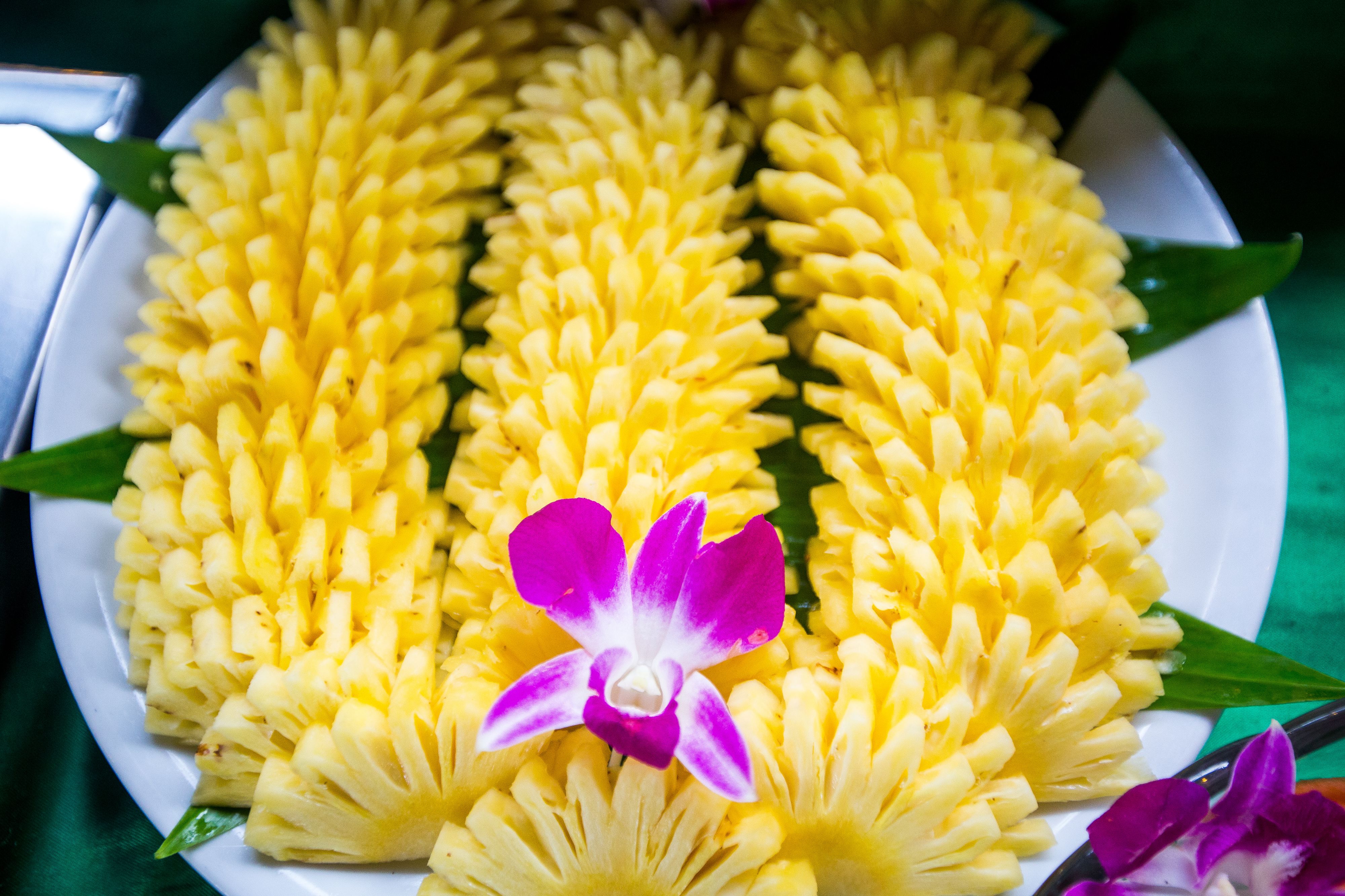 A plate of yellow pineapple slices arranged in a circular pattern with a purple orchid in the center.